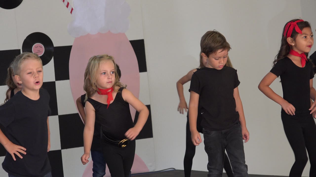 Children face forward and sideways in a dance line.