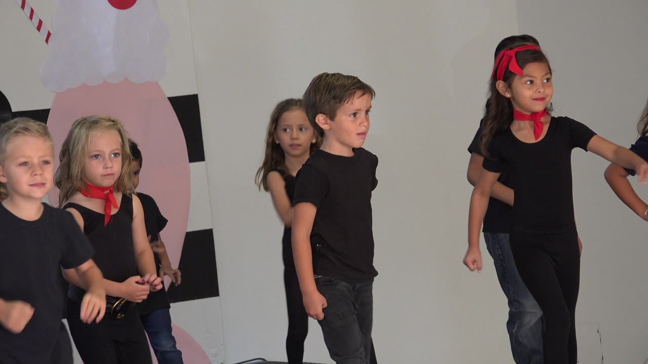 Children in black outfits stand on a decorated indoor stage.