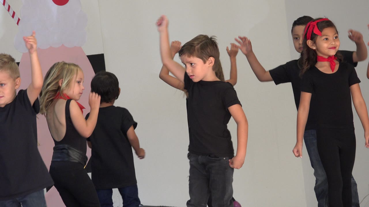 Children in black performance clothes move across the stage.