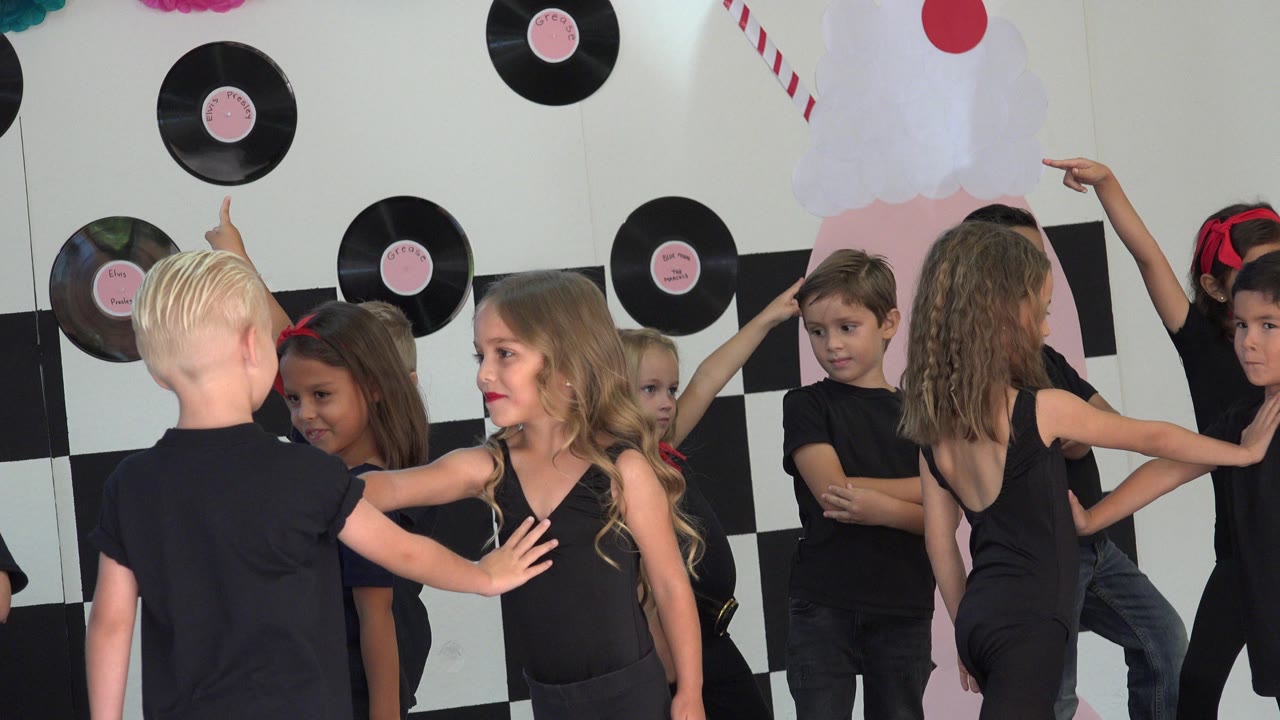 The group of children continues the routine in Cabo San Lucas, Mexico, with arms extended and several faces turned toward the camera or each other.