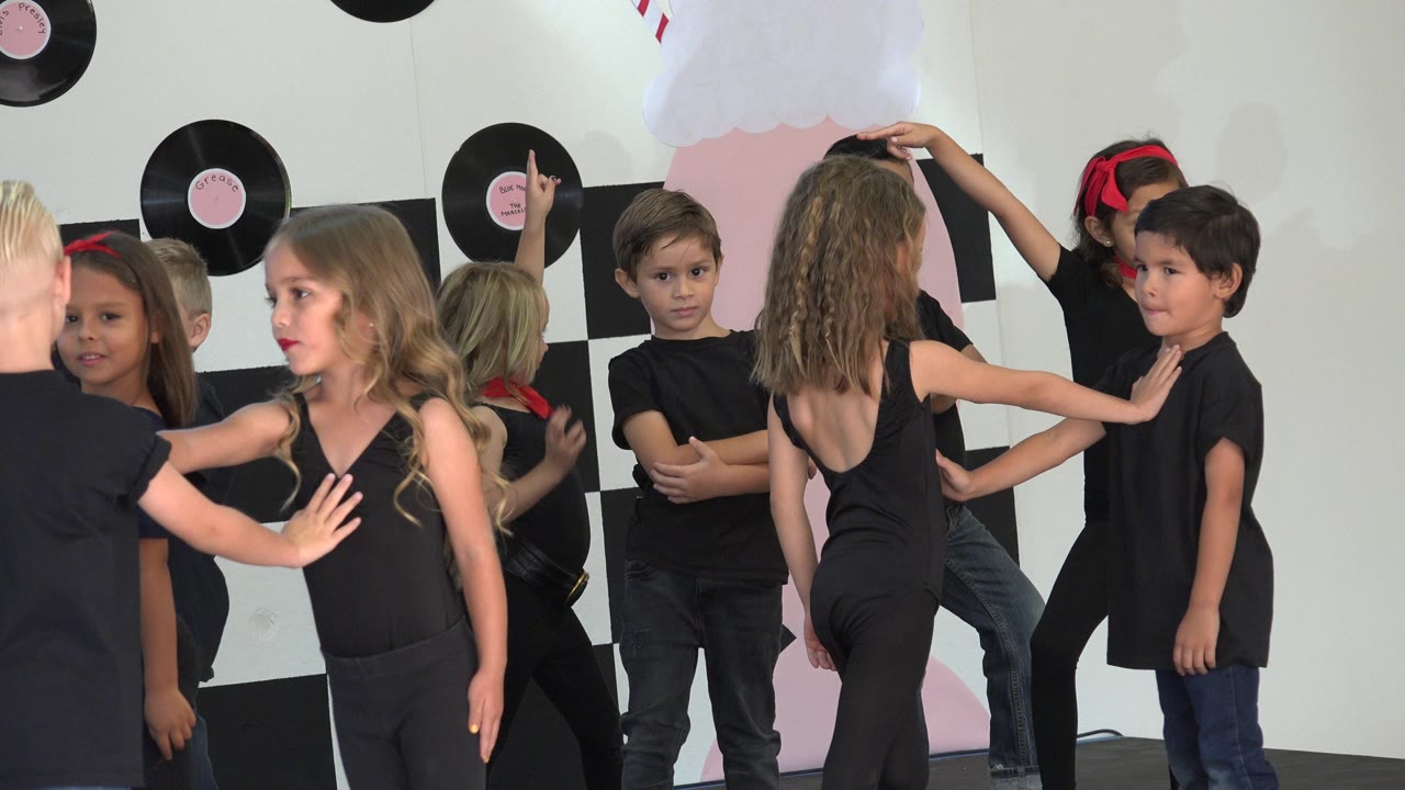 Children in black outfits rehearse in front of a checkered backdrop.