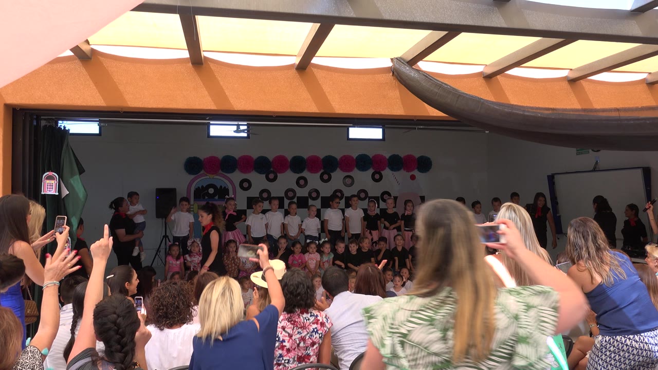 Parents raise hands and phones toward children on stage.