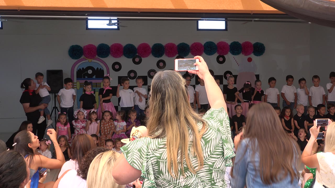 Parents filming children on an indoor school stage.