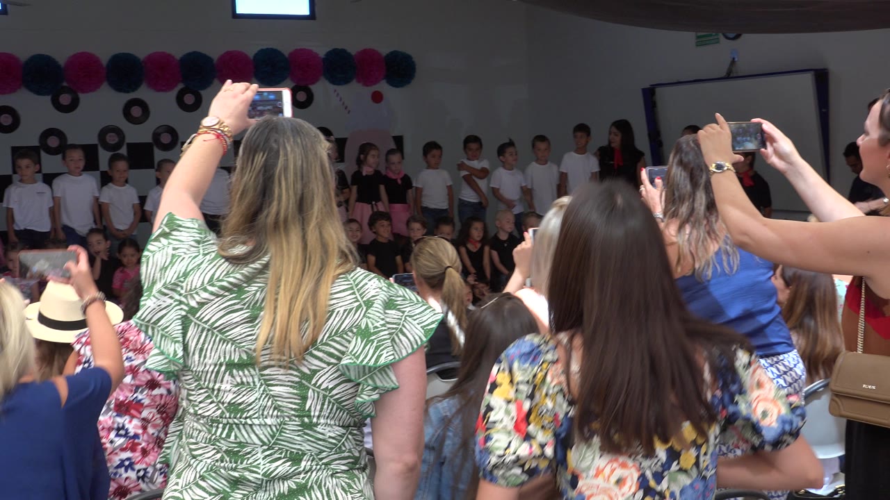 Parents stand and hold phones in the foreground while children line the back wall at an indoor Cabo San Lucas youth event.