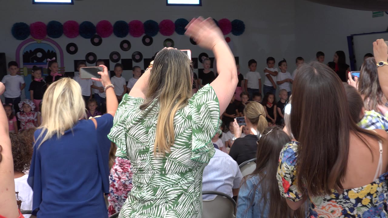 Woman waves while parents film children indoors