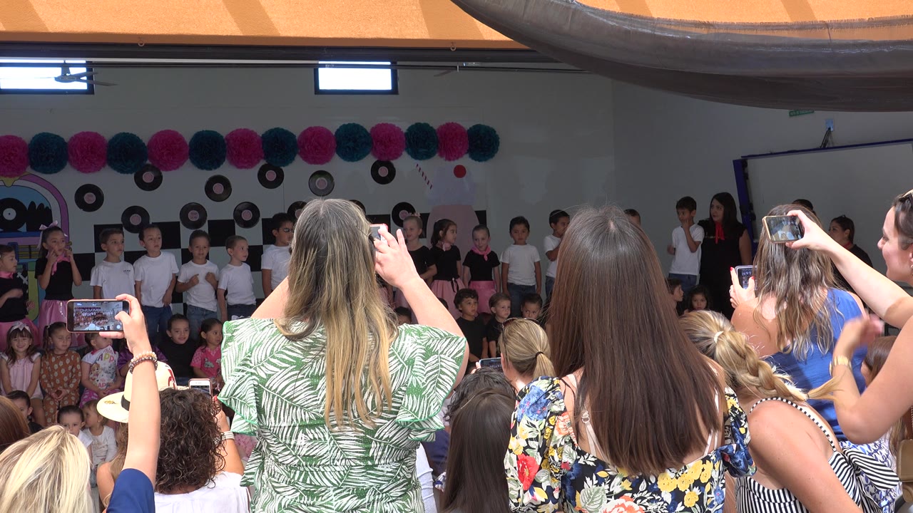 Parents filming children on an indoor school stage.