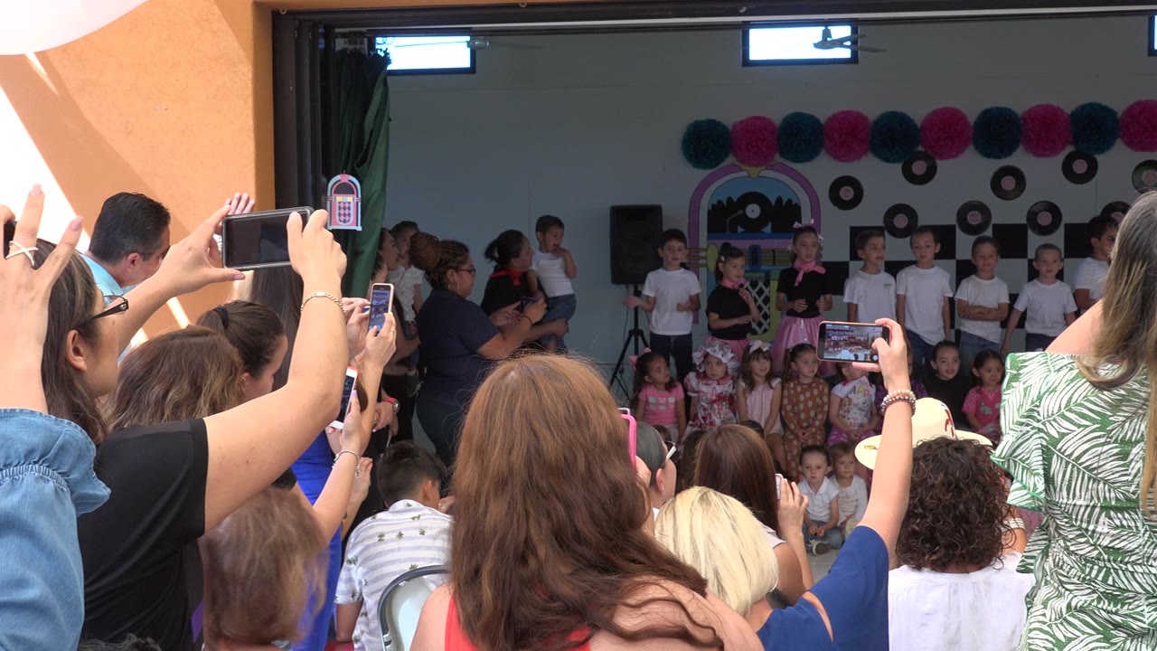 Audience members hold phones toward children on an indoor stage.