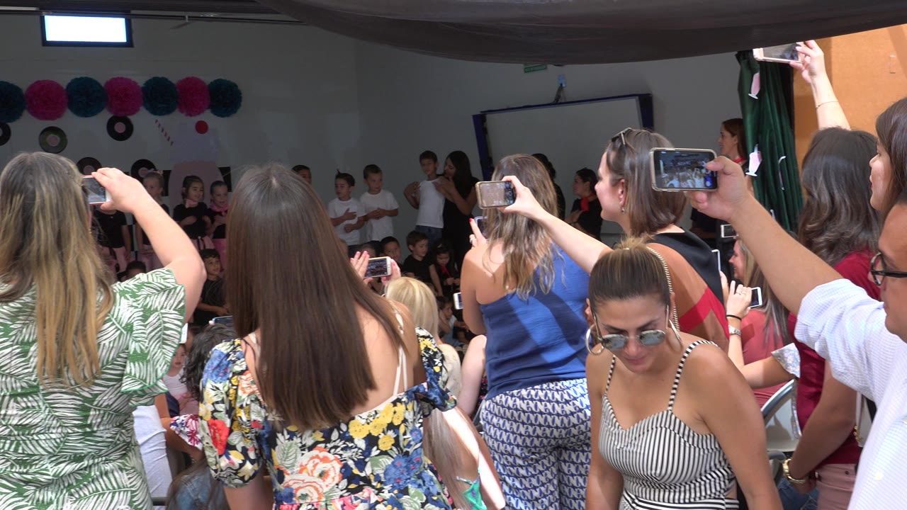 Crowded audience stands between the camera and a children's stage.