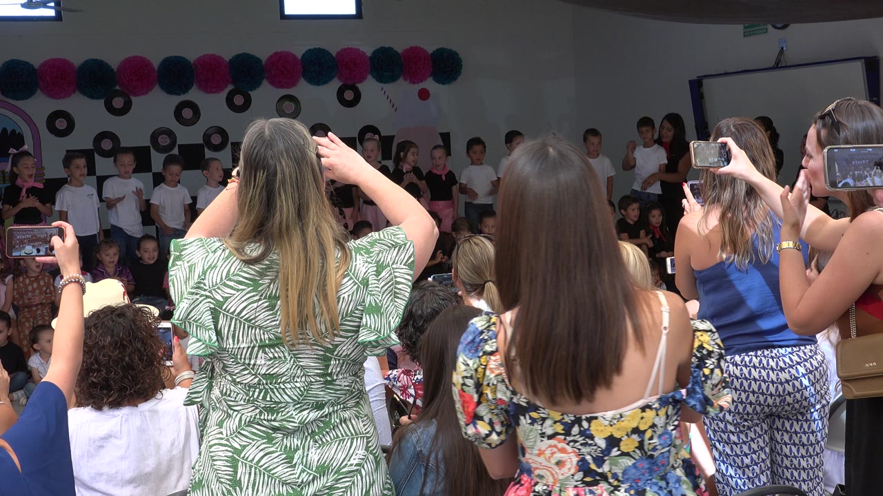 Adults recording children on an indoor stage with smartphones.