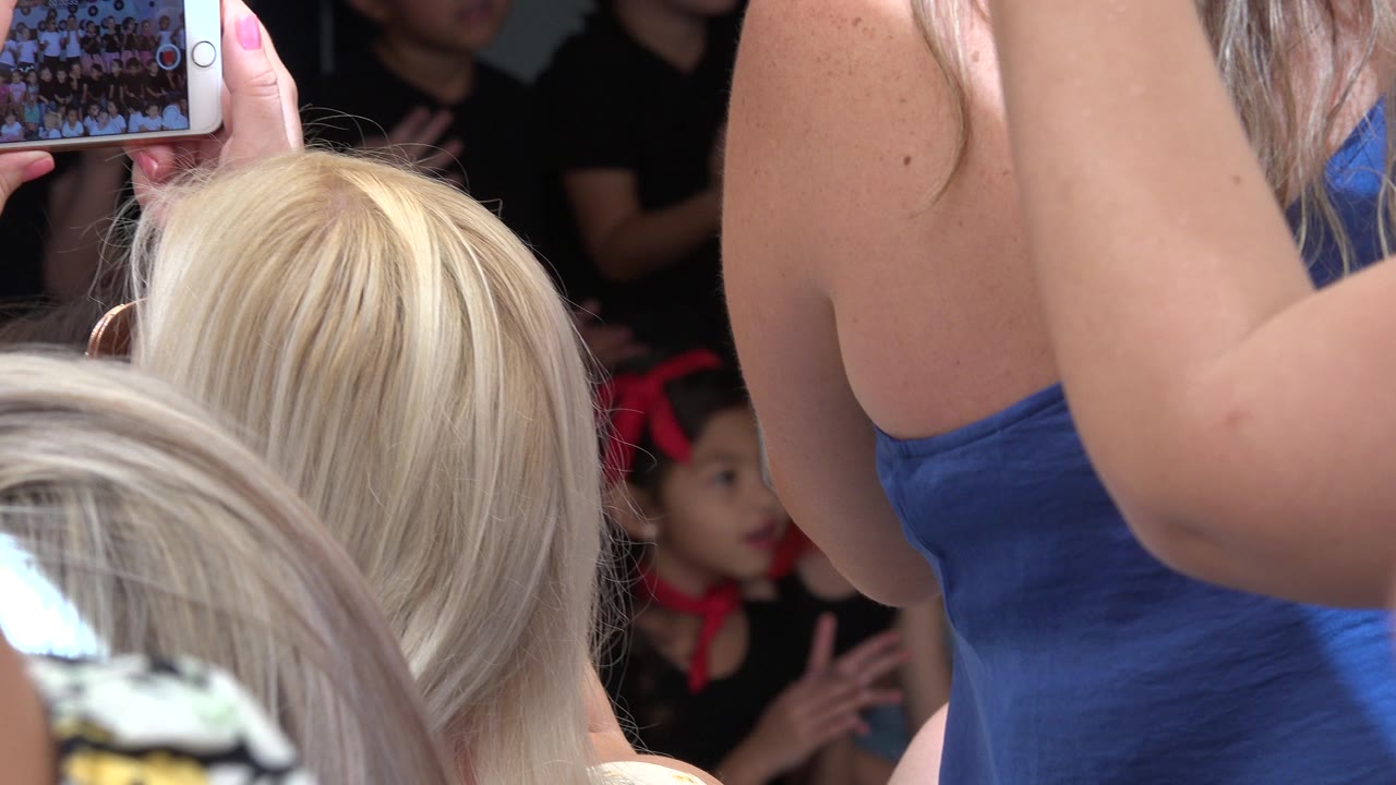 Audience phones frame a young girl standing in front of spectators.