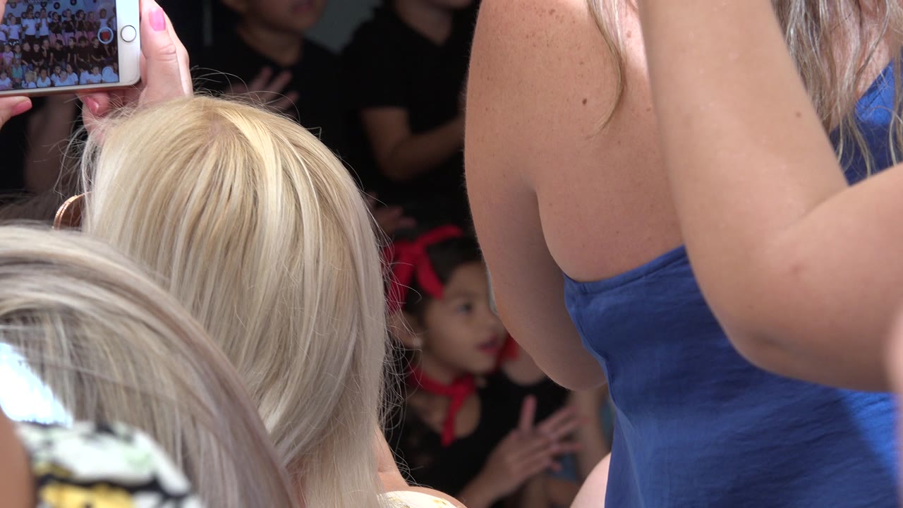 At 0:01 in Cabo San Lucas, Mexico, the girl remains in the midground as a woman in a blue top and another raised phone block much of the view.