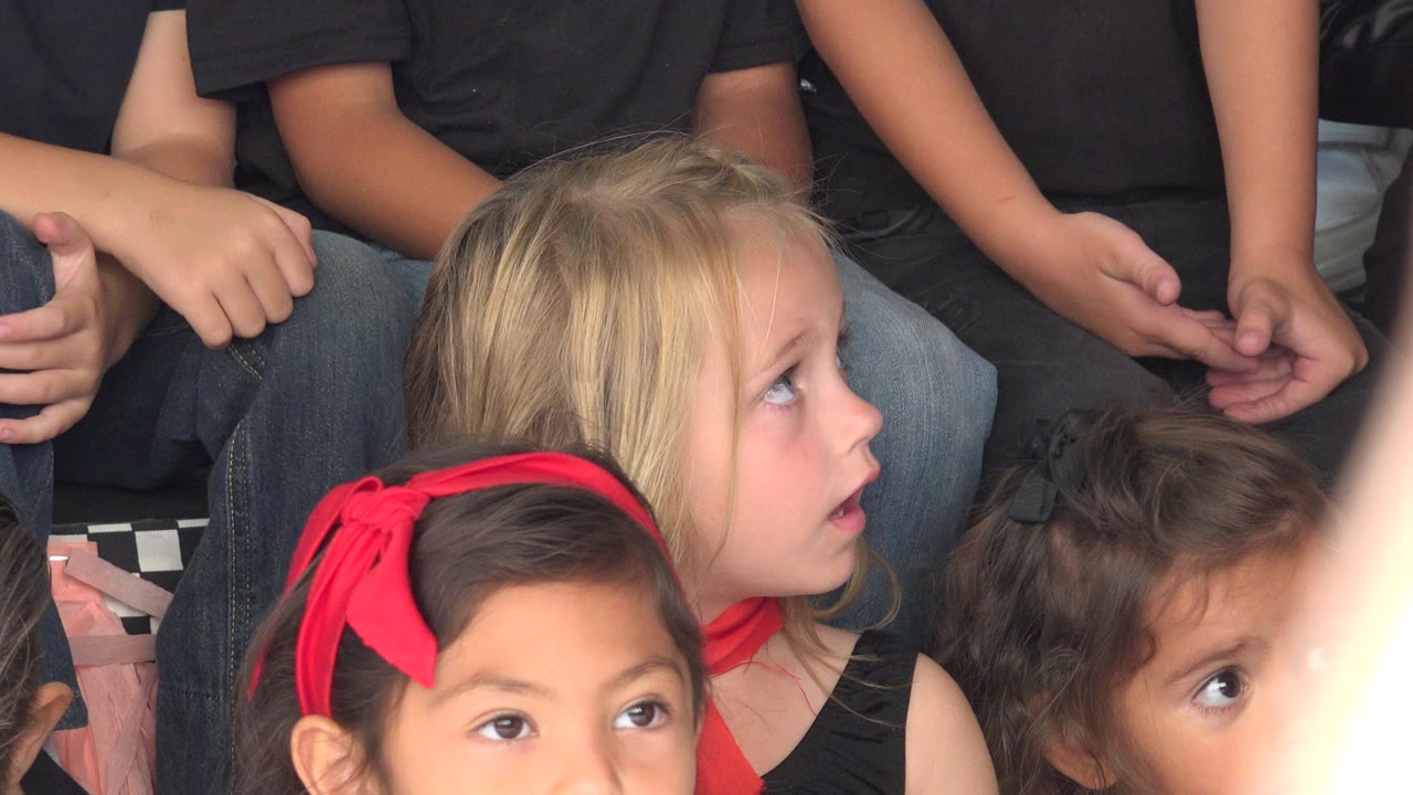 Young blonde girl looks upward among other children in black clothing.