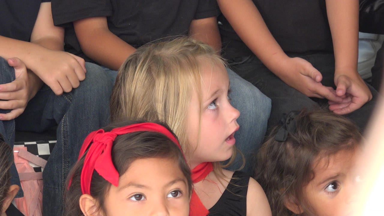 At 0:01 in Cabo San Lucas, Mexico, the blonde girl turns her gaze sideways as children in dark tops remain tightly grouped around her.