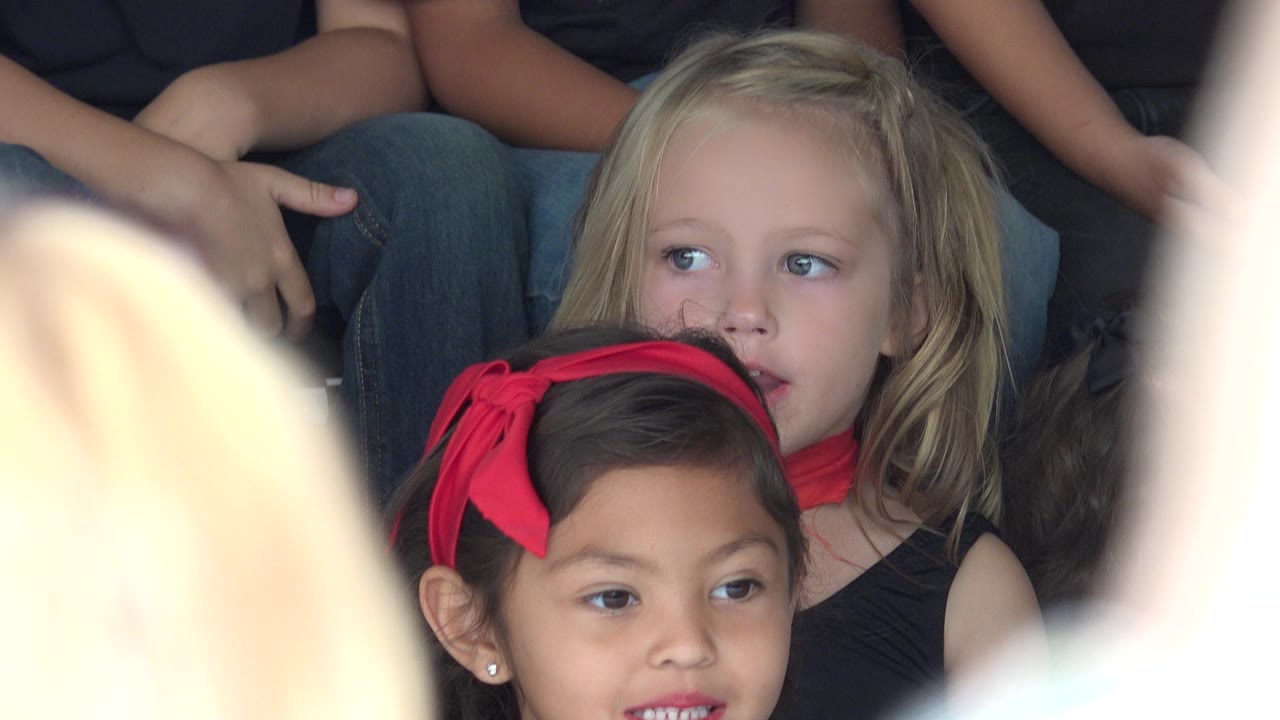In Cabo San Lucas, Mexico, the blonde child looks off to the side while the girl with the red headband remains in front, partly blocked by a bright blurred foreground shape.