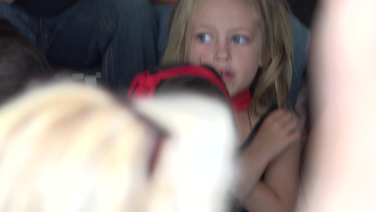 At 0:01 in Cabo San Lucas, the same blonde child remains visible behind a child with a red bow while pale foreground shapes obscure much of the lower frame.