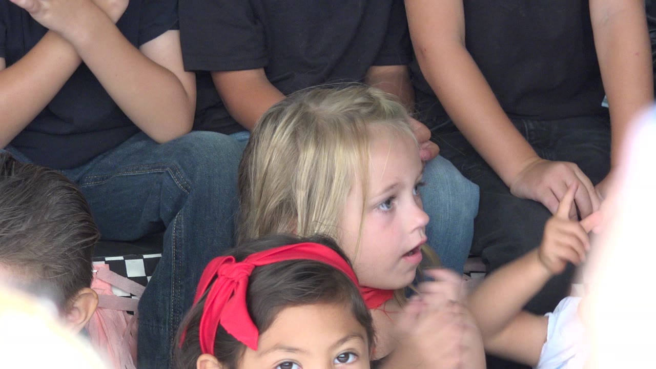 Children seated on bleachers with foreground hands partly blocking the view.