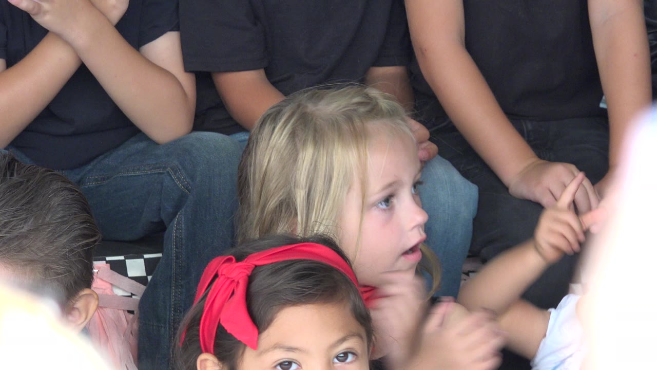 At 0:01 in Cabo San Lucas, Mexico, the same seated children remain framed tightly as the blonde child turns toward the right side and a pale raised hand obscures part of the lower image.