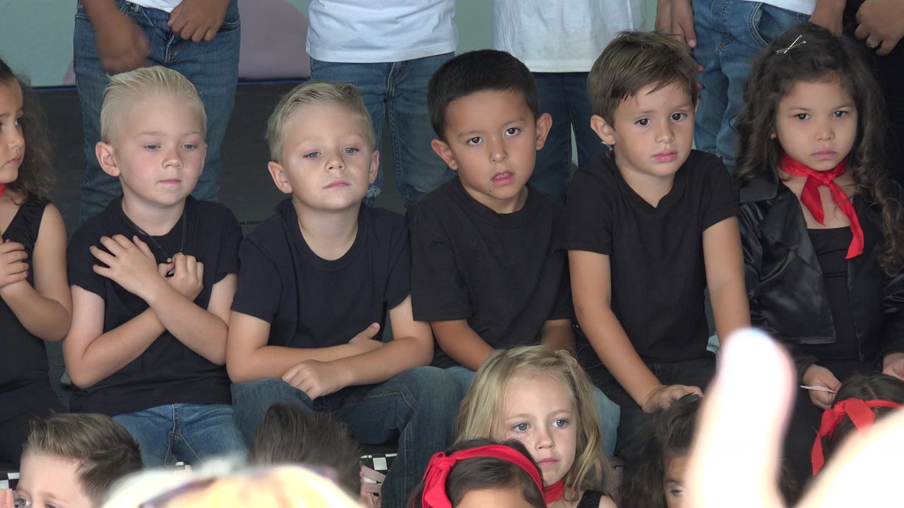 Children in black shirts seated together with adults cropped behind them.