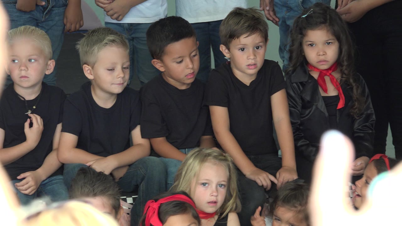 Young children in black shirts watch from a group setting.