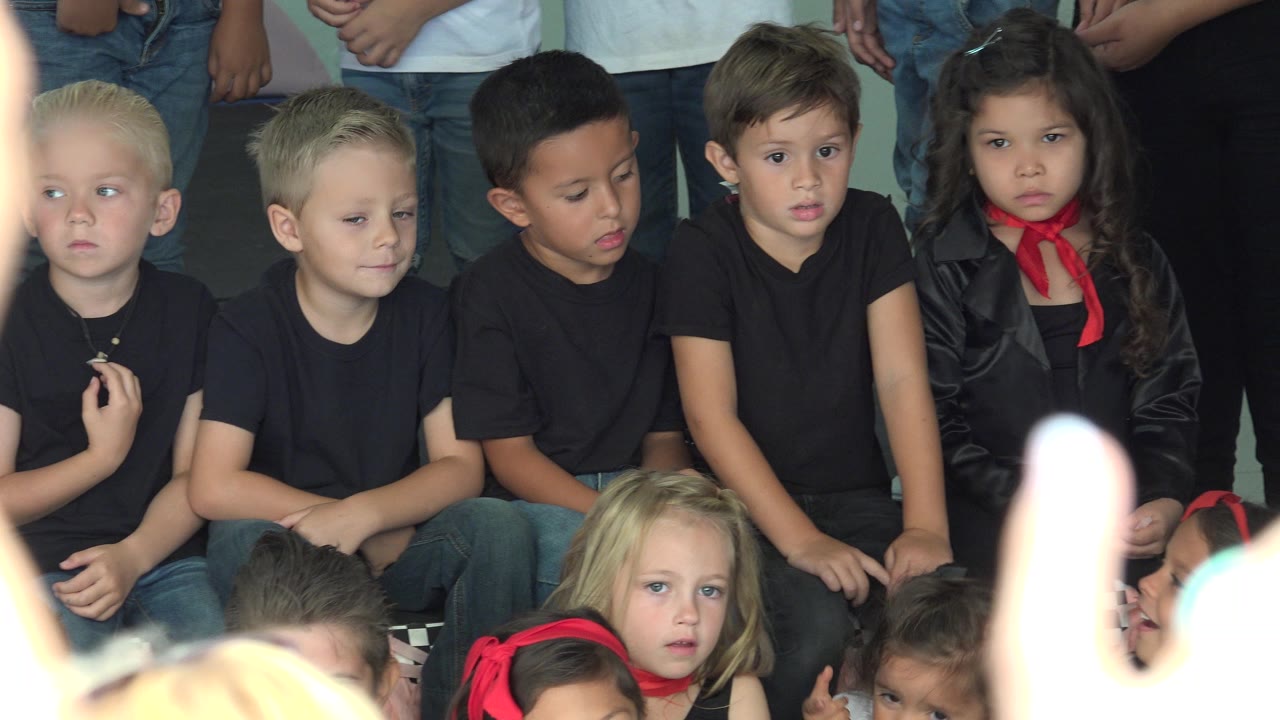 The children remain grouped in Cabo San Lucas, Mexico, with several faces turned slightly downward or sideways and a bright blurred foreground shape near the lower right.