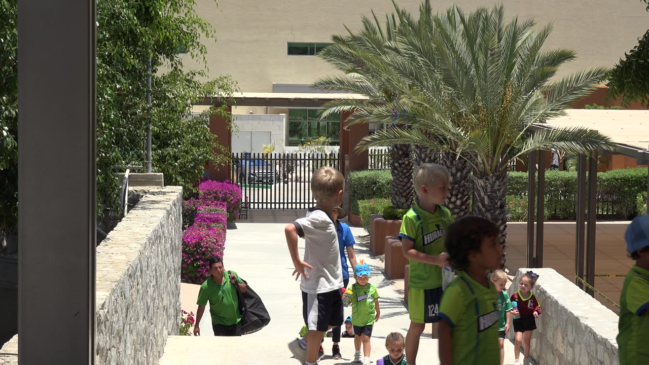 Children and adults on a sunny walkway with palm landscaping.