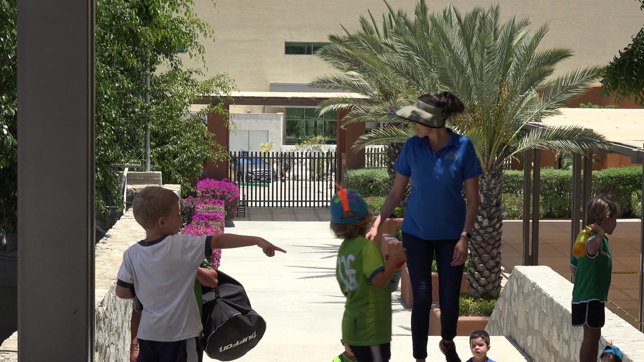 Children and an adult on outdoor steps near palm landscaping.