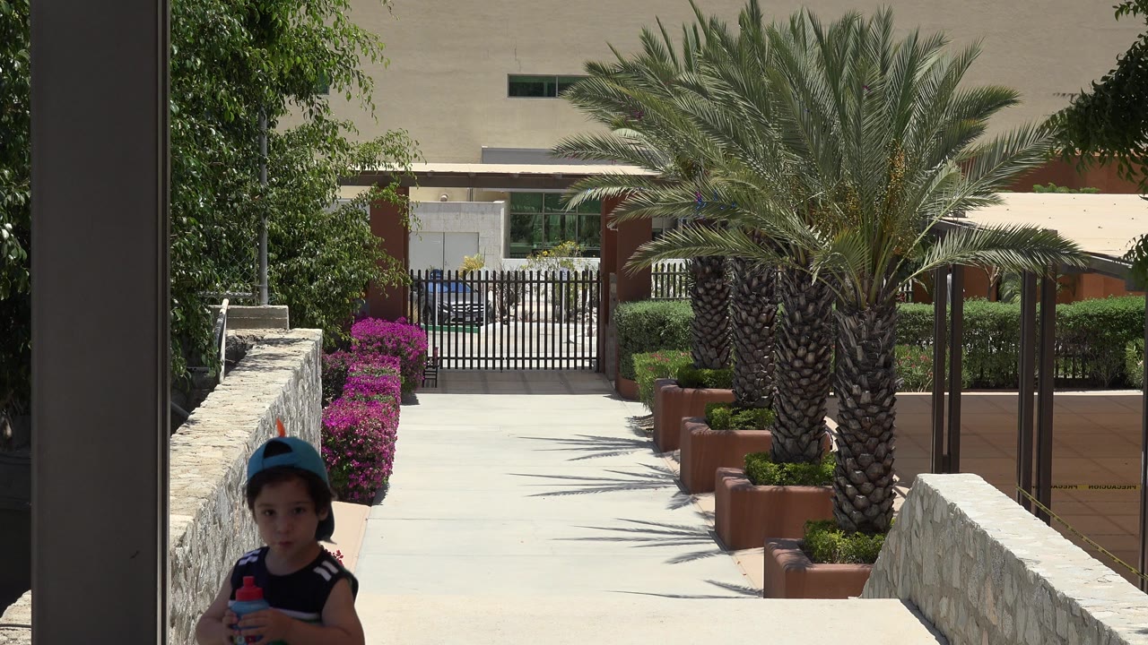 Boy in a blue cap holding a drink near a resort walkway.