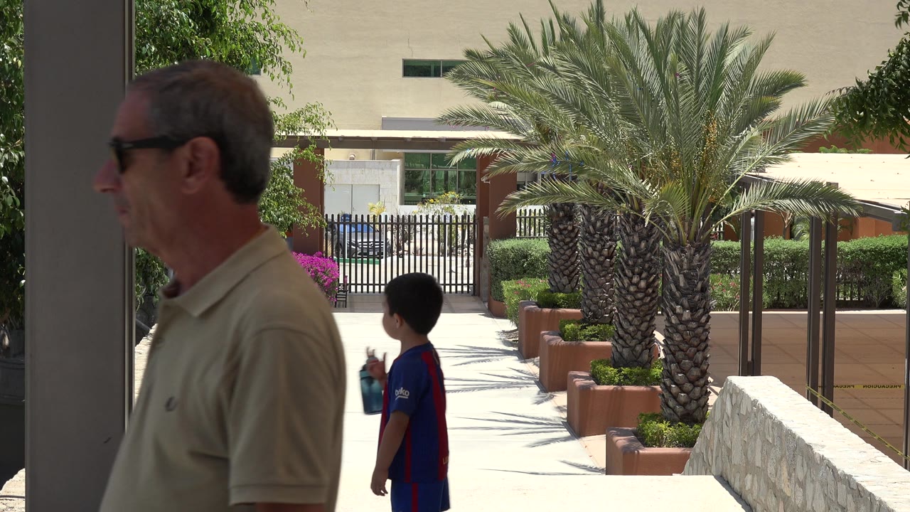 Older man and young boy in a shaded hotel walkway with palm trees beyond.