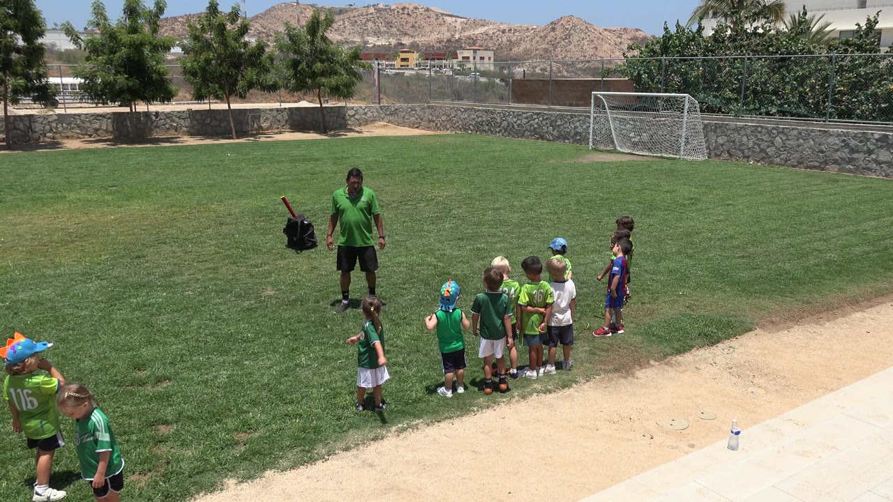 Coach facing children on a sunny grass football field.