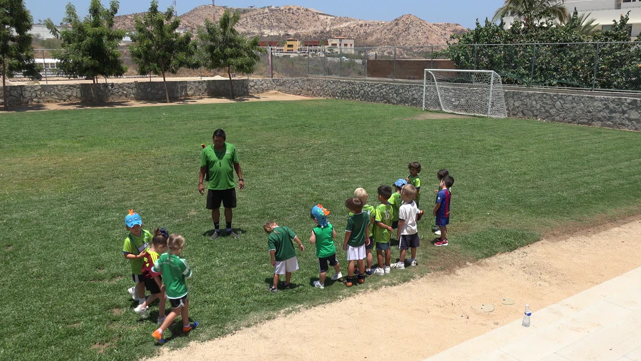 Coach and small children gather on a sunny soccer field.