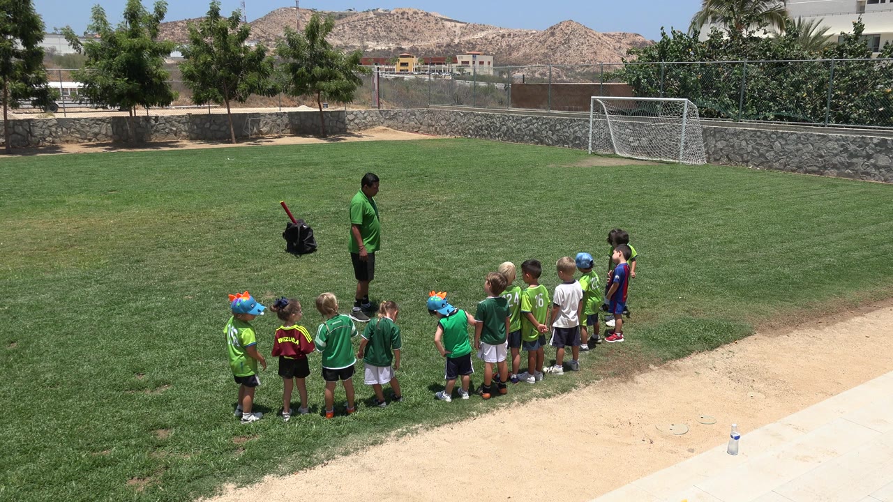 Children lined up on a grass field with an adult guide nearby.