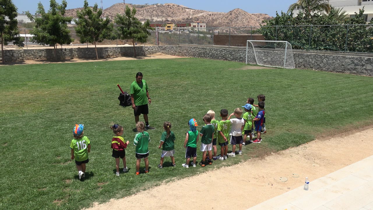 Children line up on a soccer field beside a coach in green.