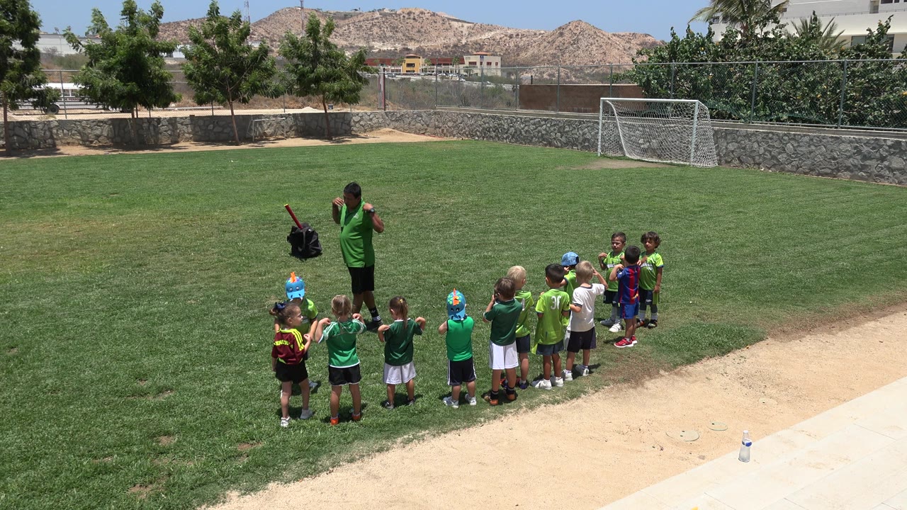 Coach stands beside children grouped on a soccer field.