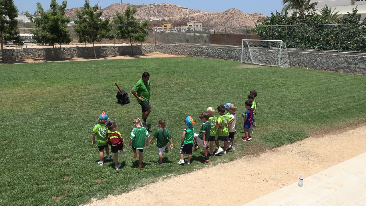 Children and a coach on a grass soccer field during warm-up.