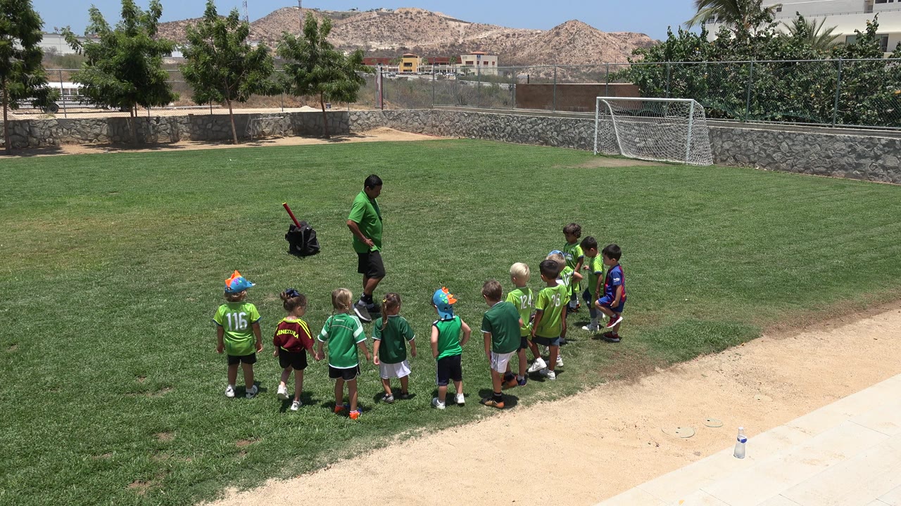 Coach stands near children lined up on a sunny soccer field.