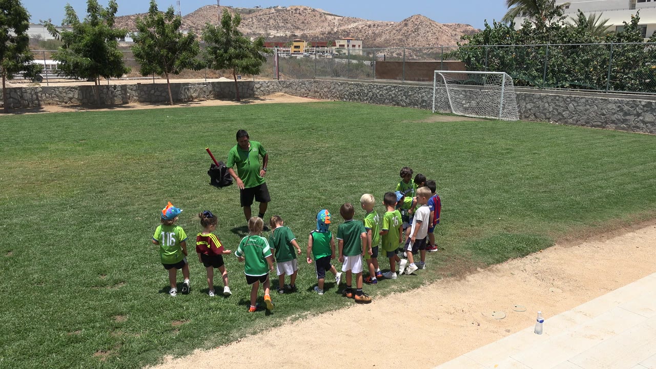 Coach gestures while children stand in a loose line on the field.