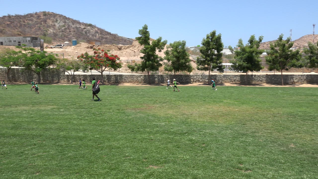 Children playing soccer on a green field with hills behind them.