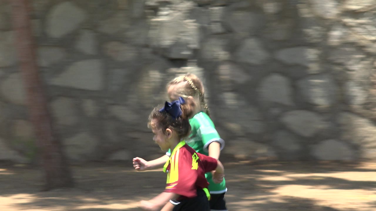 At 0:01, the girls continue running side by side in Cabo San Lucas, Mexico, with the burgundy jersey in front and the green jersey partly behind.