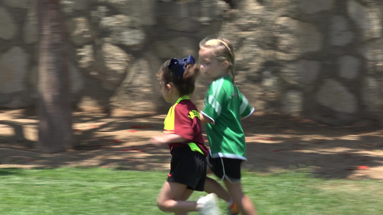 Close side view of two girls running across a sunny grass field.