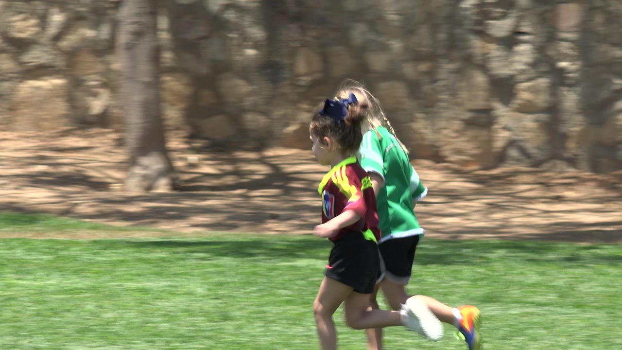 The girls remain side by side while running in Cabo San Lucas, Mexico, with their bright shirts and shoes standing out against the grass.