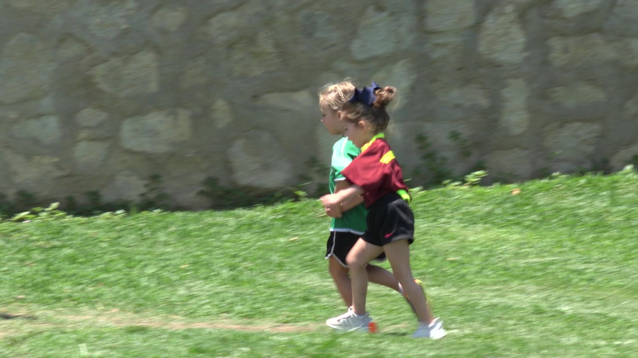 Two young children in sports shirts running on grass.