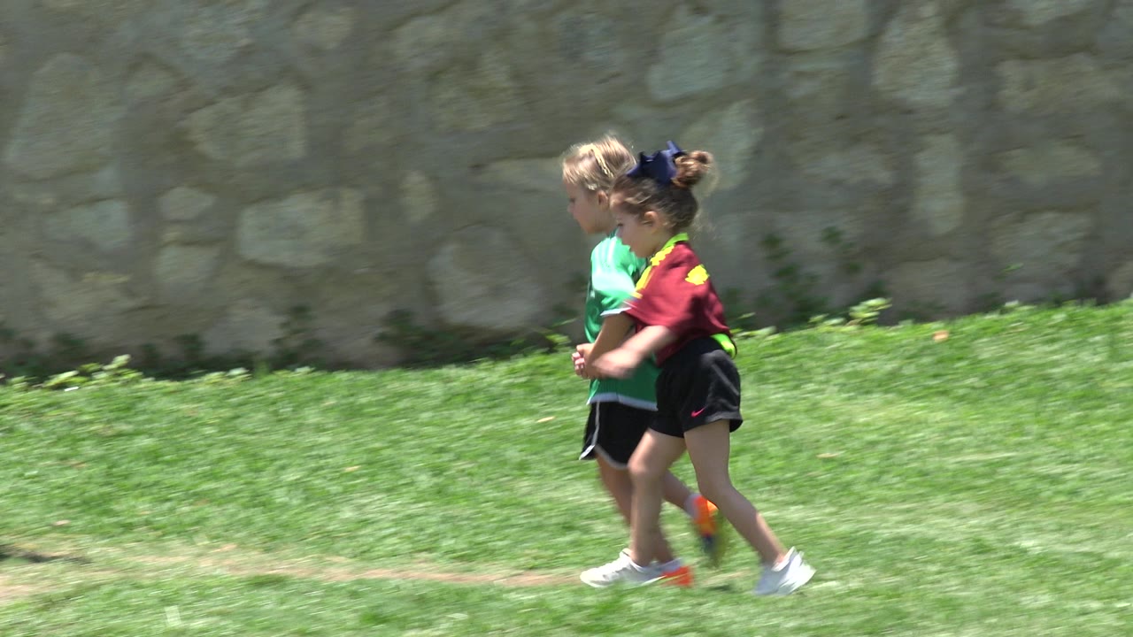 The children continue running side by side on the lawn in Cabo San Lucas, Mexico, with the stone wall still filling the background.