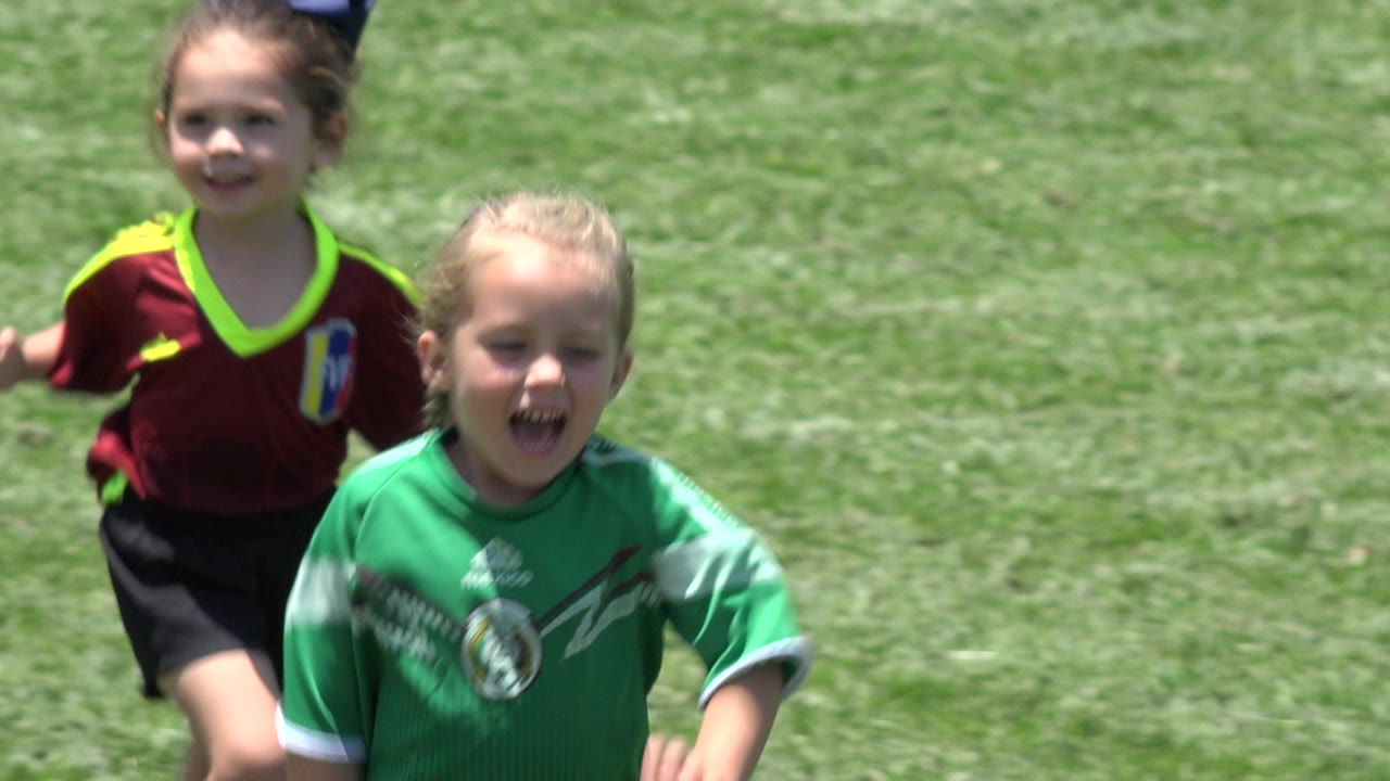 The girl in a green Mexico soccer shirt runs in front while the girl in red follows behind on the grass in Cabo San Lucas, Mexico.