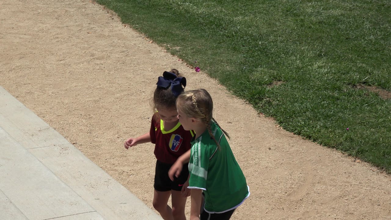 The girls remain close on the concrete steps, with the green jersey in front of the red jersey and grass behind them in Cabo San Lucas, Mexico.