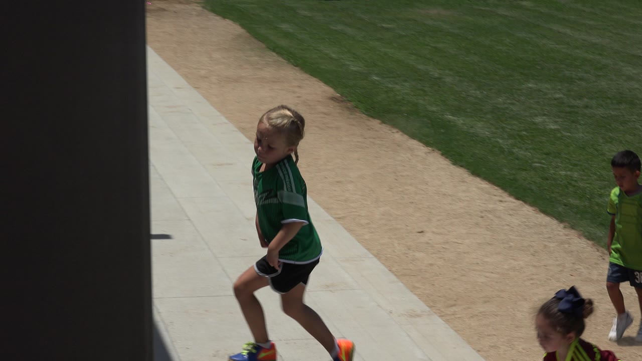 Child in green soccer jersey walking near a field-side path