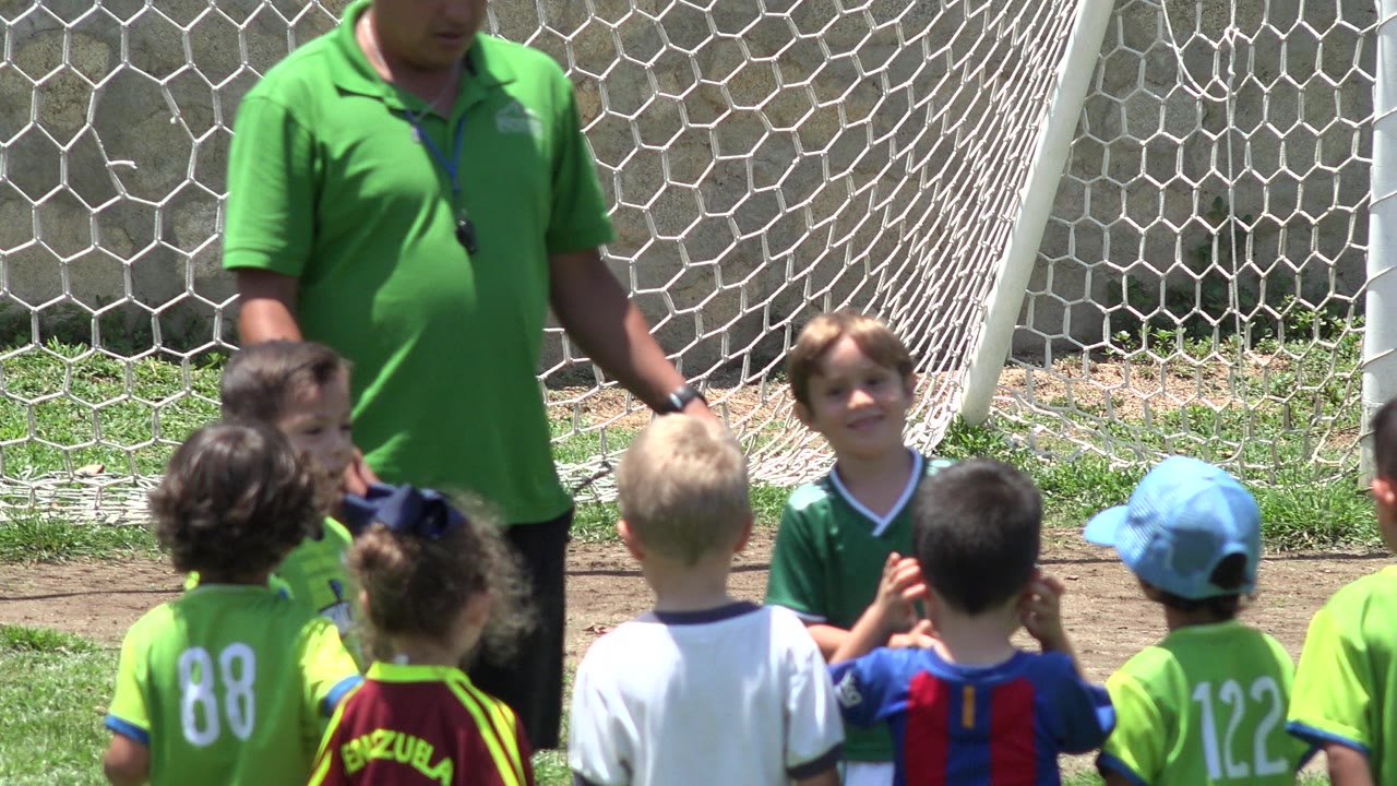 Coach stands beside children in soccer jerseys near a goal net.
