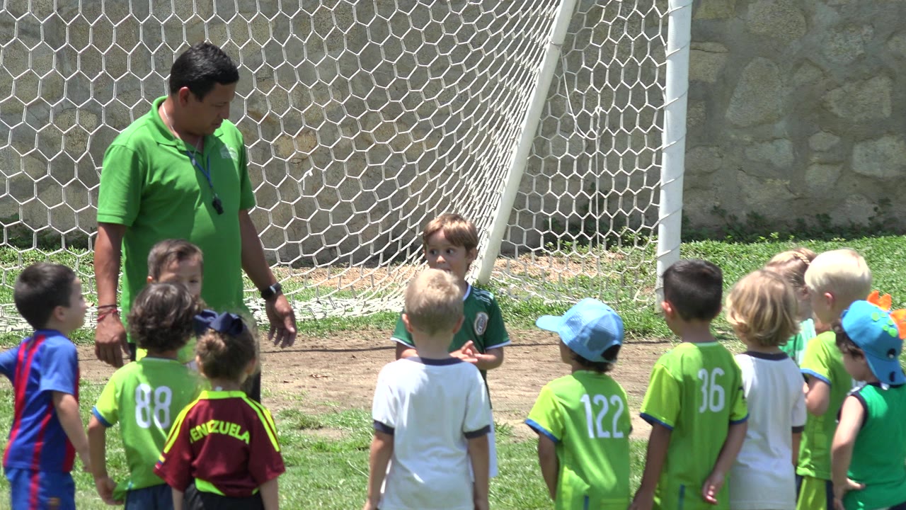 Coach standing beside young children on a soccer field.
