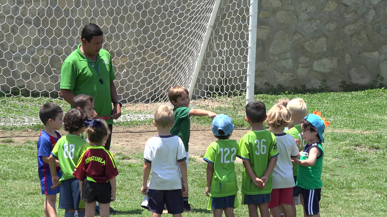 Coach standing with children near a soccer goal on a grass field.