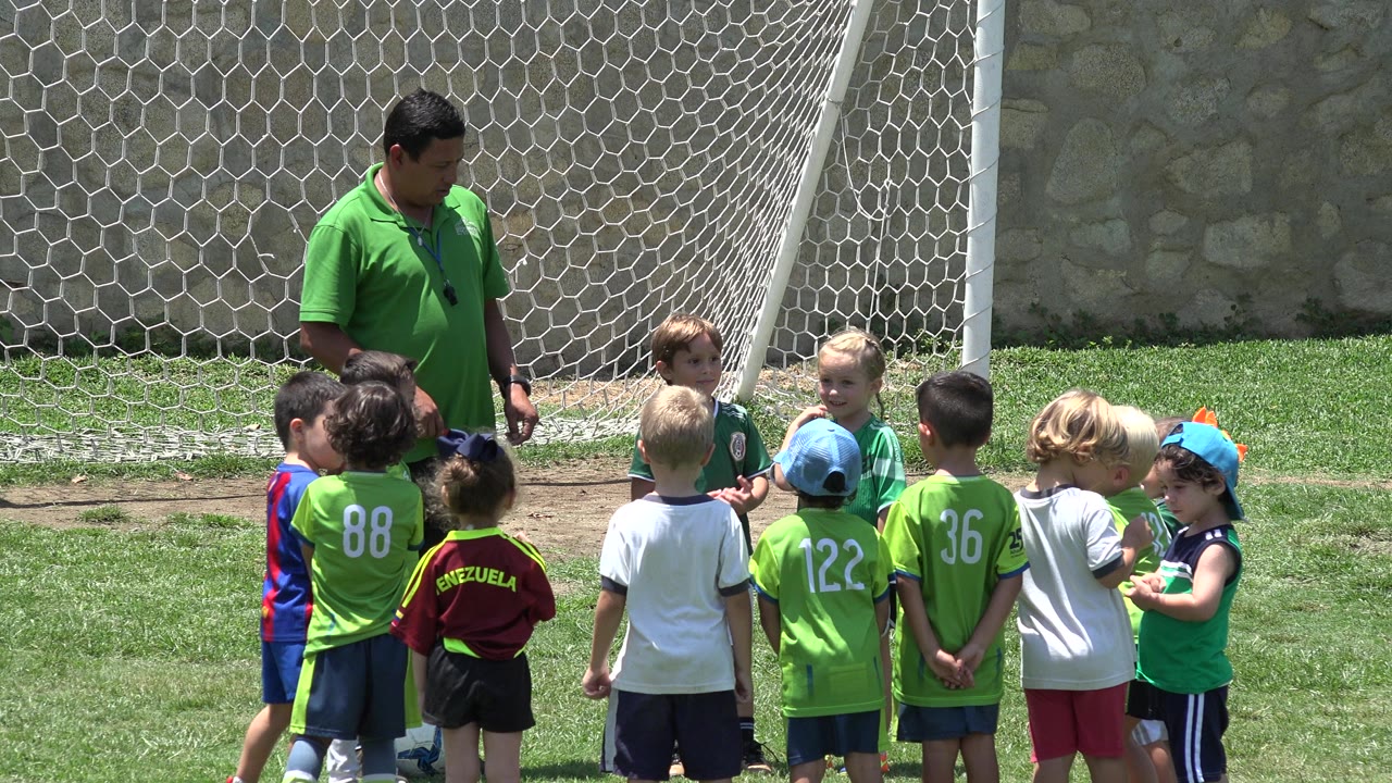 In Cabo San Lucas, Mexico, children in green and white soccer clothes stand in a loose semicircle as the coach looks down toward them near the goal.