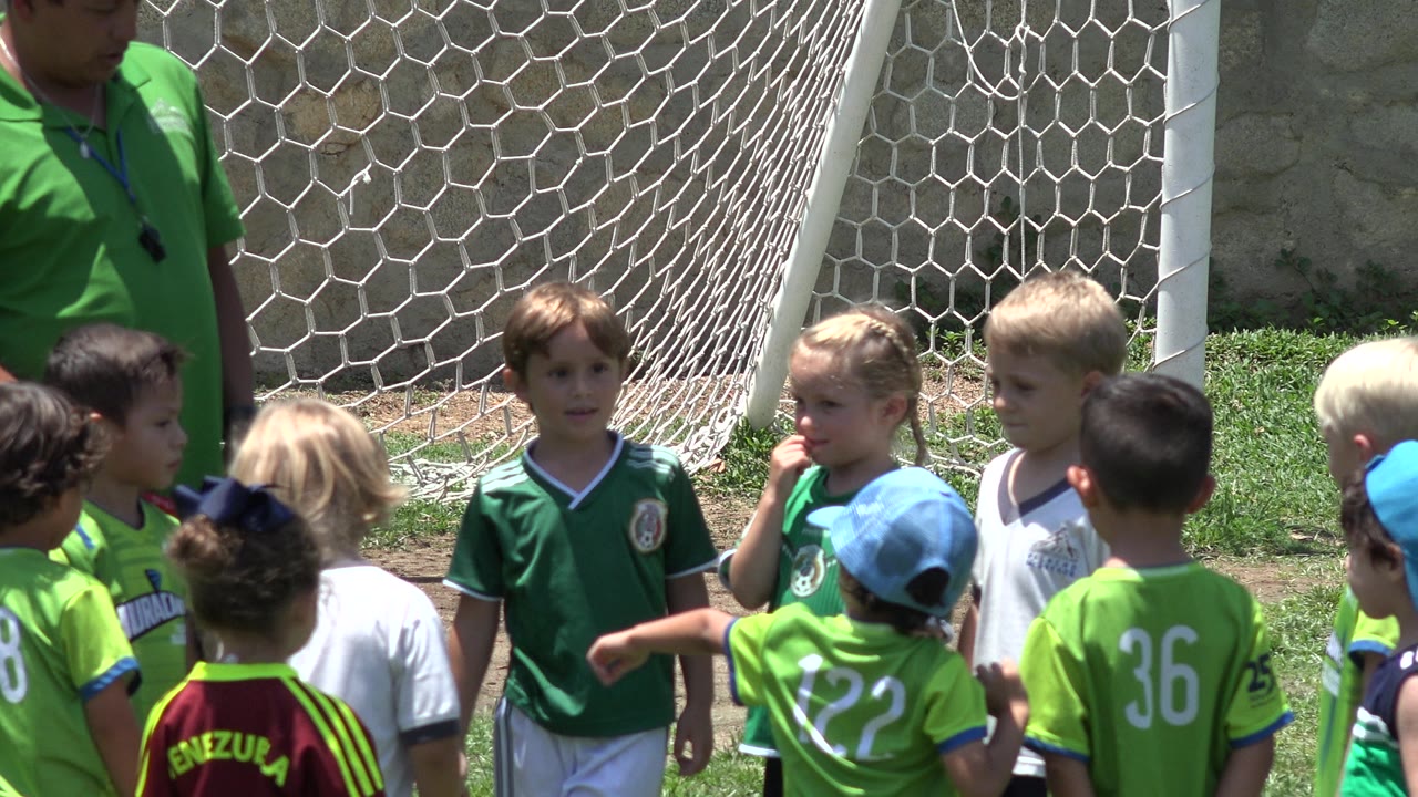 A child in a green Mexico jersey stands among other children by a goal net.